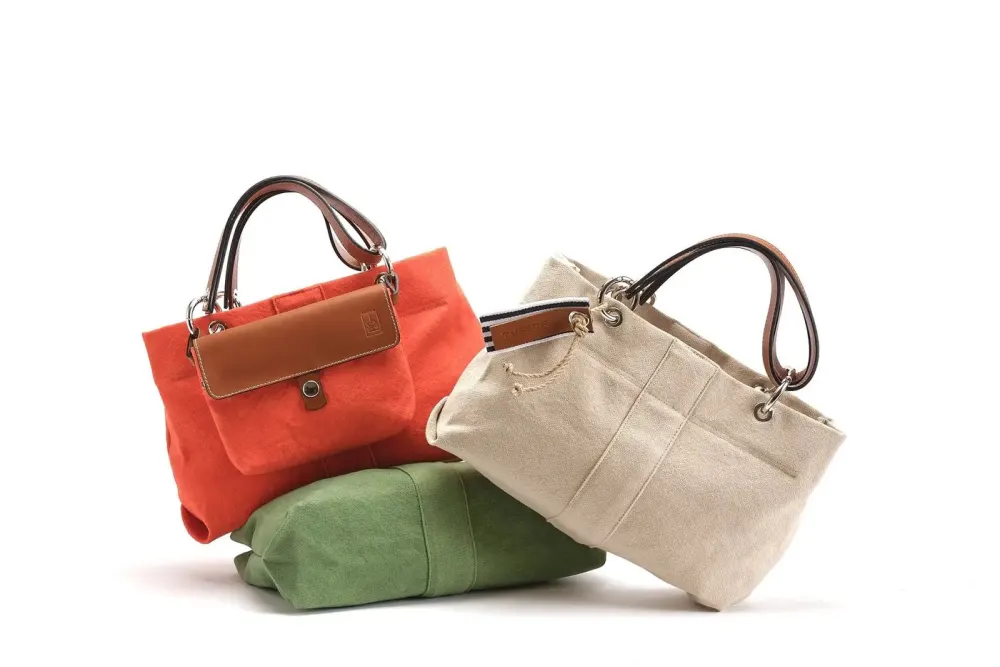 Deux sacs à main en toile avec anses en cuir, l’un orange et l’autre beige, posés sur un sac vert.